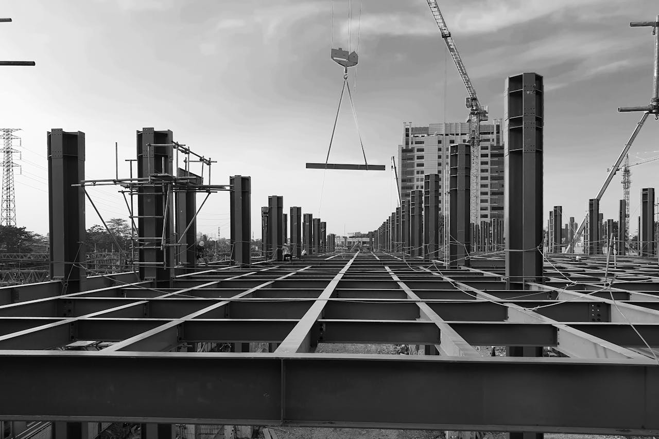 Black and white view of a modern urban construction site in Indonesia with steel beams and cranes against a cloudy sky.